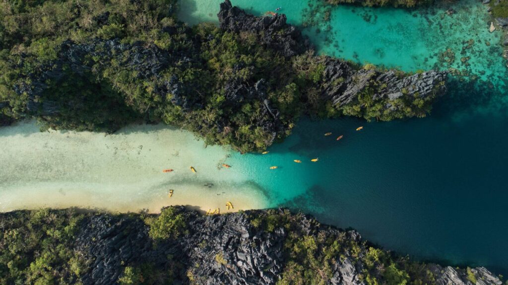 Aerial view of kayaks on turquoise waters between rocky, forested islands.