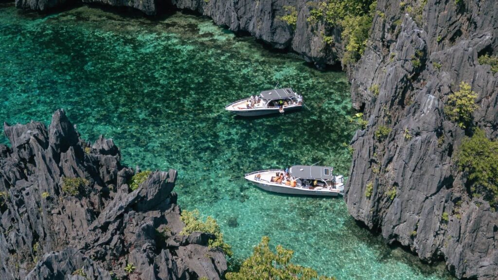 Two boats in clear turquoise water surrounded by rocky cliffs.
