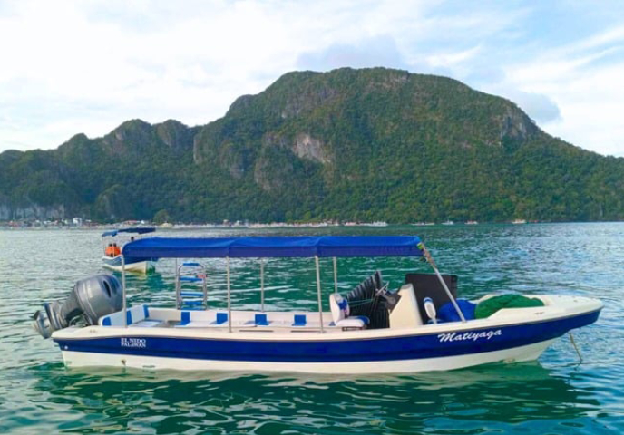A blue and white motorboat named "Matiyaga" on the water, with a lush green island in the background.