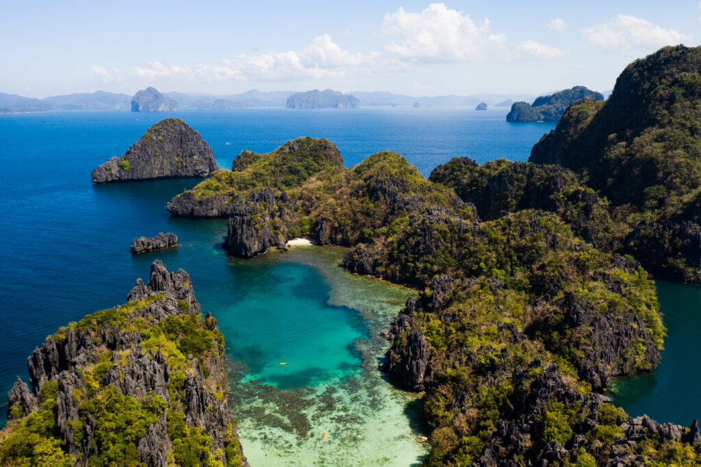 Aerial view of a tropical beach cove in El Nido, Palawan, Philippines, surrounded by lush islands and turquoise water.