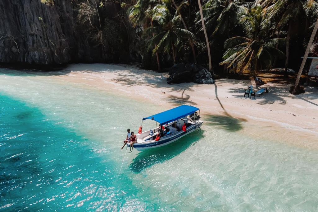 Aerial view of a boat on a tropical beach with turquoise water and palm trees.