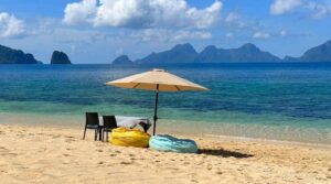 Beach scene with umbrella, chairs, beanbags, and distant islands.