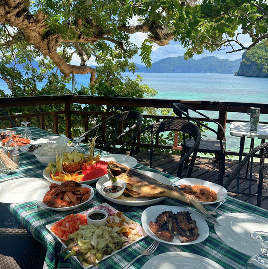 A table laden with food on a deck overlooking a tropical ocean view.